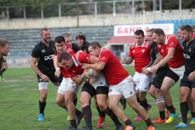 ODESSA, UKRAINE -20.10.17 - Ukrayna ragbi şampiyonası finali CREDO (Odessa) - kırmızı, OLYMPIK (Kharkiv) siyah rugby oyuncularının top için yoğun mücadelesi. Yeşil sahada dinamik bir oyun. Acımasız ragbi