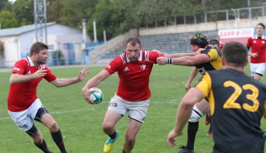 ODESSA, UKRAINE -20.10.17 - Ukrayna ragbi şampiyonası finali CREDO (Odessa) - kırmızı, OLYMPIK (Kharkiv) siyah rugby oyuncularının top için yoğun mücadelesi. Yeşil sahada dinamik bir oyun. Acımasız ragbi