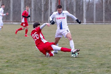 ODESSA, Ukrayna 02.24.2021 - FC Chernomorets (beyaz) Odessa yerel FC Real Pharma kulübüyle şehir şampiyonasında bir araya geldi. Futbolcular futbol stadyumunun çimlerinde topla hareket halindeler