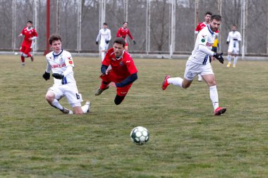 ODESSA, Ukrayna 02.24.2021 - FC Chernomorets (beyaz) Odessa yerel FC Real Pharma kulübüyle şehir şampiyonasında bir araya geldi. Futbolcular futbol stadyumunun çimlerinde topla hareket halindeler