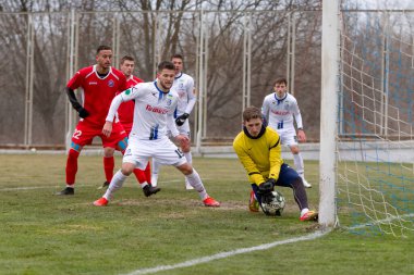 ODESSA, Ukrayna 02.24.2021 - FC Chernomorets (beyaz) Odessa yerel FC Real Pharma kulübüyle şehir şampiyonasında bir araya geldi. Futbolcular futbol stadyumunun çimlerinde topla hareket halindeler