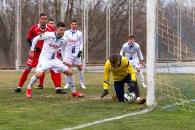 ODESSA, Ukrayna 02.24.2021 - FC Chernomorets (beyaz) Odessa yerel FC Real Pharma kulübüyle şehir şampiyonasında bir araya geldi. Futbolcular futbol stadyumunun çimlerinde topla hareket halindeler