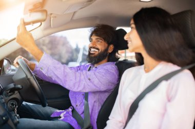 Kadın bakarken gülümseyen Hintli adam dikiz aynasını ayarlıyor. Güvenli sürüş alışkanlıklarını, günlük konuşmaları ve bir yolculukta ilişki uyumunu gösterir, yakın plan.
