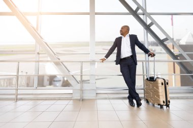 Kendinden emin Afrikalı Amerikalı işadamı, elinde bavulla havaalanı penceresinin önünde duruyor. Yatmadan önce dışarıya gülümsüyor, sakin ve başarılı bir yolcu gibi bakıyor.