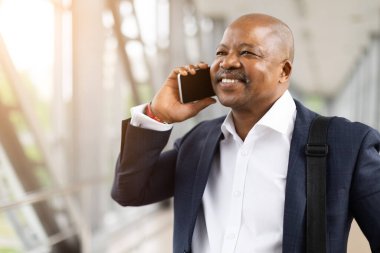 Havaalanı terminalinde telefon görüşmesi yapan Afro-Amerikan bir işadamı. Güvenle gülümsüyor, donanma kıyafeti giyiyor ve omuz çantası taşıyor. Yola çıkmaya hazır.