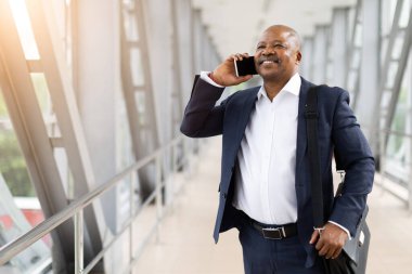Kendine güvenen Afrikalı Amerikalı işadamı telefonda konuşuyor, havaalanı koridorunda evrak çantası taşıyor, iş seyahatinde ya da toplantıda gülümsüyor ve rahatlıyor.