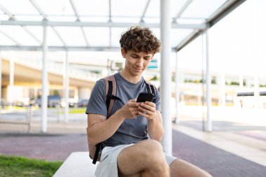 Havaalanı bankında oturan genç adam akıllı telefon kullanıyor, ekrana, mesajlaşmaya ya da internete odaklanmış. Yolculuk veya uçuştan önce sakin bir bekleme anı