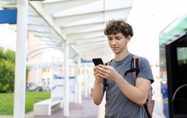 Havaalanı otobüs terminalinde akıllı telefonunu kullanan genç bir adam kalkışı beklerken kitap okuyor ya da mesaj yazıyor. Yolculuktan önce sakin bir an.