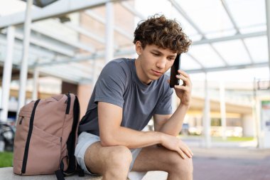 Havaalanında oturmuş akıllı telefondan konuşan ciddi bir genç adam odaklanmış bir ifadeyle aşağıya bakıyor. Endişeli seyahat çağrısı ya da sevinç sorunları kavramı