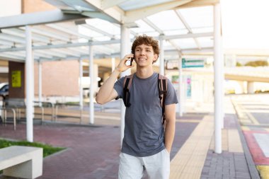 Gezgin adam havaalanı yolunda sırt çantasıyla dolaşırken telefon görüşmesi yapıyor. Parlak gün ışığı ve pozitif iletişim anı