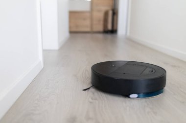 Akıllı robot elektrikli süpürge koridorda hareket ediyor. Modern ev otomasyon cihazı günlük yaşam alanlarının verimli bakımı için özerk temizlik sağlar