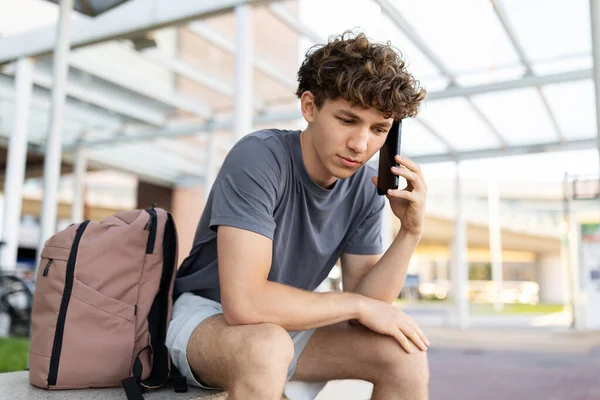 Havaalanında oturmuş akıllı telefondan konuşan ciddi bir genç adam odaklanmış bir ifadeyle aşağıya bakıyor. Endişeli seyahat çağrısı ya da sevinç sorunları kavramı