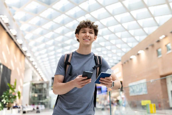 Havaalanında elinde akıllı telefon ve pasaportla gülümseyen genç bir adam. Heyecanlı yolcu giriş veya uçuş için hazır, terminalde duruyor, kopyalama alanı