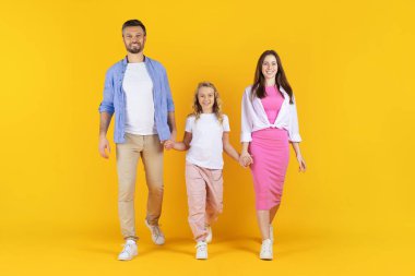 Gülümseyen aile sarı arka planda stüdyoda birlikte yürüyor. Parlak renklerde giyinmiş, neşe ve birlik içinde el ele tutuşan ebeveynler ve kızlar, boşluğu kopyalayın.