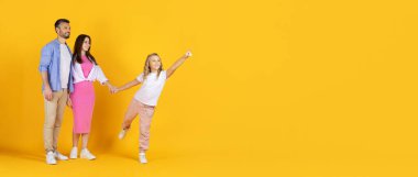 Mutlu aile sarı arka planda bekliyor, kızı heyecanlı bir şekilde işaret ediyor. Aile görüşü, iyimserlik ve neşeli birlikteliğin sembolü, kopyalama alanı