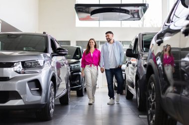 Galerideki yeni arabaların arasında el ele yürüyen gülümseyen genç bir çift. Neşeli alıcılar, neşeli ve kendine güvenen araçları keşfediyorlar.