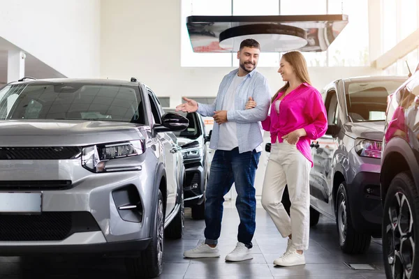 Satıcıda karısının araba özelliklerini gösteren mutlu bir adam. Genç çift araç seçeneklerini tartışıyor, galeride yeni araba deneyiminin tadını çıkarıyor.