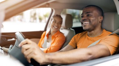 Mutlu genç siyah çift birlikte araba sürerken rahat bir anın tadını çıkarıyor, Afrikalı Amerikalı eşler gülüyor ve otomobillerin içinde eğlenceli sohbetler ediyorlar.