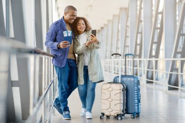 Seyahat sigortası konsepti. Havaalanında uçuşunu bekleyen mutlu ve genç Afrikalı bir çiftin portresi, ellerinde pasaport tutan ve Terminal 'de beklerken bilet kontrol eden mutlu, genç bir Afrikalı çiftin portresi, kopyalama uzayı. Yüksek kalite fotoğraf