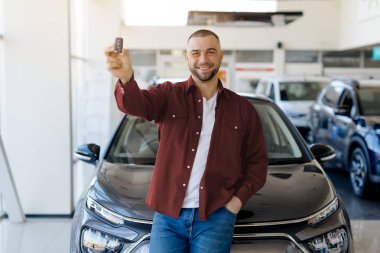 Otomobilin anahtarını elinde tutan yakışıklı bir adam, galeriden yepyeni bir araba alıyor. Mutlu milenyum erkeği yeni bir araba alıyor, siyah arabaya yaslanıyor ve anahtarı kameraya gösteriyor, boş alan.