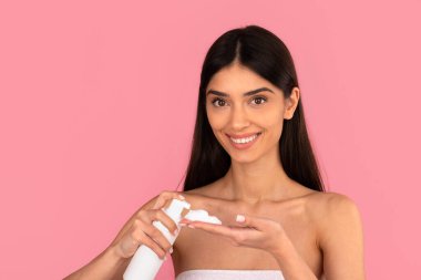 Gülümseyen kadın köpük temizleyiciyi eline alıp cilt temizleme rutinine hazırlanıyor. Pembe stüdyo arka planında güzellik, hijyen ve yüz temizliği kavramı
