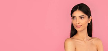 Temiz ciltli, gülümseyen genç bir kadın pembe arka plana bakıyor. Stüdyo portresi taze güzelliği, sağlığı ve kendi kendine bakım konseptini temsil ediyor.