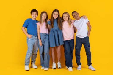 Genç öğrenciler birbirlerine yakın duruyorlar ve sarı stüdyo arka planında güvenle poz veriyorlar. Bir grup arkadaş canlısı çocuk birlik, dostluk ve modern okul yaşam tarzı gösteriyorlar.
