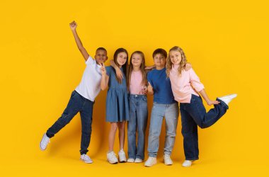 Sarı stüdyo arka planında farklı jestler yapan neşeli bir grup genç öğrenci. Mutlu çocuklar dostluk, birlik ve hayat dolu bir okul hayatı gösteriyorlar.