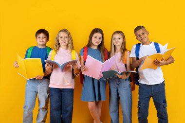 Parlak stüdyo arka planında açık kitaplar okuyan bir grup genç öğrenci. Gülümseyen çocuklar öğrenmeyle ilgileniyorlar ve pozitif bir okul hayatı tarzını temsil ediyorlar.