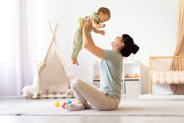 Anne bebeğini neşeli bir şekilde evdeki aydınlık odada kaldırarak neşeli ve enerjik bir bağ yaratıyor. Neşeli etkileşim aşkı, güveni ve neşeli aile hayatını vurgular.