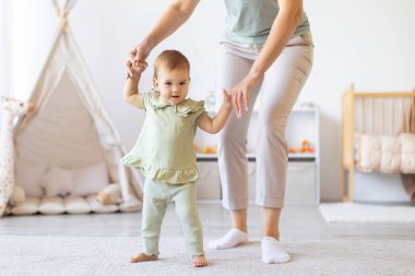 Bebek ilk adımlarını çalışırken annelerinin elini tutuyor. Erken çocukluk gelişiminin öğrenme, denge, destek ve sıcak bağlantısını yakaladığı an