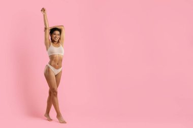 Full length pose of young black woman in beige underwear on pink studio background. Fit physique, natural confidence and modern lifestyle concept for fashion and wellness themes