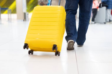 Sarı bavulu kapat ve yetişkin bir adamın yürüdüğü havaalanında yuvarlan. Hareket kabiliyeti, bagaj taşımacılığı ve modern terminal ortamını gösteren seyahat taşımacılığı kavramı