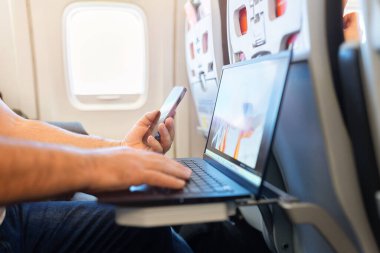 Uçak uçuşu sırasında akıllı telefon ve dizüstü bilgisayar kullanan yolcu. Mobil teknoloji, iletişim ve uçuş verimliliği kavramına sahip modern dijital seyahat tarzı