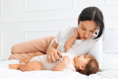 Anne, bebeğini evde bir yatakta yatarken gıdıklıyor. Neşe, etkileşim ve rahatlamış aile yaşam tarzıyla neşeli ebeveynlik anı