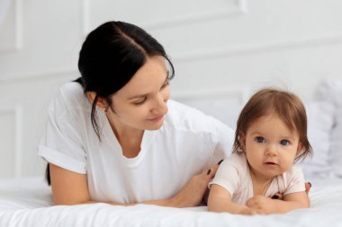 Anne, karnında bir yatakta bebeğine göz kulak oluyor. Gündüz vakti güven, bakım ve aile hayatı ile sıcak ebeveynlik anı