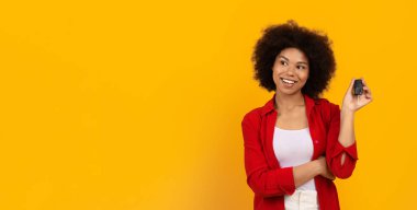 Sarı arka planda gülümseyen ve elinde araba anahtarı olan Afrikalı genç bir Amerikalı kadın araba satın alma, araç kiralama, taşınabilirlik, ulaşım ve yaşam tarzı başarısı kavramı..