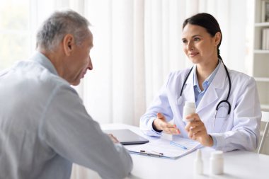 Kadın doktor, klinikteki üst düzey erkek hastaya danışmanlık yapıyor. Parlak modern sağlık bürosundaki tıbbi randevu sırasında ilaç ve tedavi planını anlatıyor.