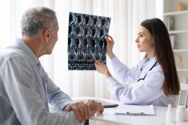 Tıbbi konsültasyon, radyoloji teşhisi ve sağlık hizmetleri konsepti sırasında yaşlı erkek hastaya omurilik röntgeni görüntüsünü açıklayan kadın doktor