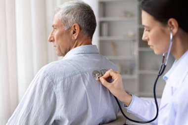 Üst düzey erkek hastaları muayene eden kadın doktor, muayenede steteskopla muayene eden kadın, klinikte randevusu sırasında olgun bir erkeğin nefesini dinleyen terapist kadın.