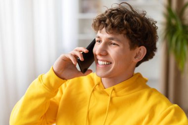 Evde akıllı telefondan konuşan gülümseyen genç adama yakın çekim, olumlu sohbet, modern yaşam tarzı ve içerideki dijital iletişim kavramı