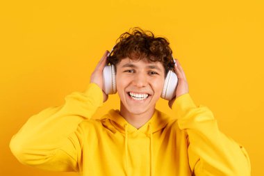 Mutlu genç adam kablosuz kulaklık takıyor ve sarı arka planda gülümsüyor, müzikten, ses eğlencesinden ve pozitif duygularla rahat modern yaşam tarzından hoşlanıyor.