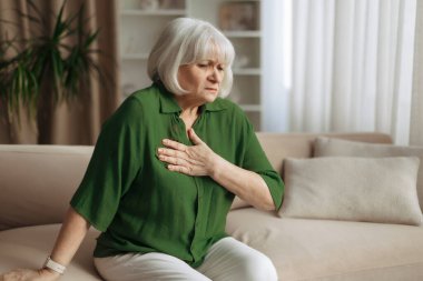 Beyaz kadın öne eğiliyor ve göğsüne dokunuyor, yaşlı kadın nefes darlığı çekiyor ya da acı çekiyor, sağlık hizmetleri ve yaşlanan yaşam tarzı kavramı içeride.