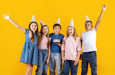 Doğum günü pastası ve parti şapkalarıyla poz veren bir grup gülümseyen ergen çocuk sarı stüdyo arka planında kutlama yapıyorlar. Neşeli çocukluk hayatı imajı