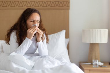 Hasta beyaz kadın yatakta oturup burnunu mendille siliyor, grip ya da alerji belirtileri gösteriyor, ev hastalıkları, sağlık ve iyileşme konsepti kapalı alanda.