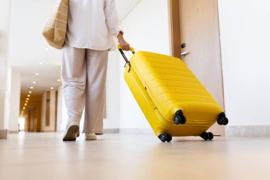 Yetişkin beyaz bir kadının otel koridorunda sarı bavulu çekişi, seyahat ve hareketlilik konsepti, modern iç mekan, yaşam tarzı turizmi ve konukseverlik.