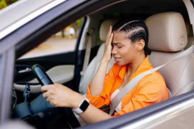 Alnında stres ya da baş ağrısı olan, her gün işe gidip gelirken zorlanan ve duygusal açıdan rahatsız edici bir şekilde araba süren siyahi kadın.