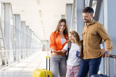 Havaalanında üç kişilik bir aile uçuştan önce pasaportları kontrol ediyor, aile tatilinden önce belgeleri hazırlıyor ve heyecanlı bir tatil deneyimi yaşıyor.