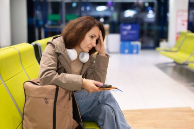 Stresli beyaz kadın gezgin havaalanında bekliyor. Kulaklıkları boynunda. Uçak kalkmadan önce telefon ve belgeleri kontrol ediyorlar.