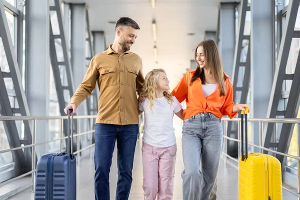 Aileler kızlarıyla havaalanı terminalinde yürüyor, gülümsüyor ve renkli bavullarıyla aile tatili seyahatinin tadını çıkarıyorlar, uçuşa hazırlar.